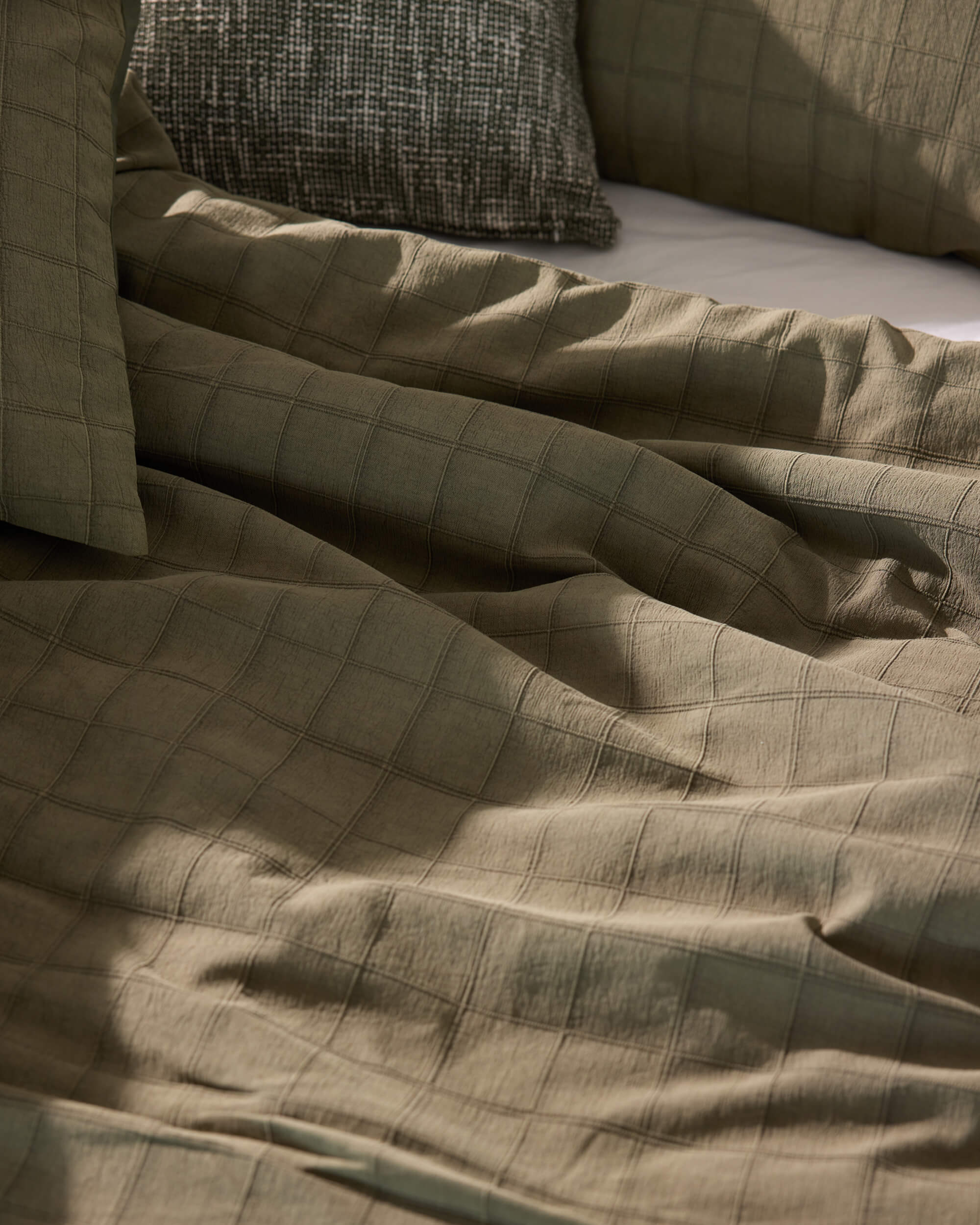 Royal Doulton Eirian olive green checked duvet cover styled with matching pillows and a textured cushion