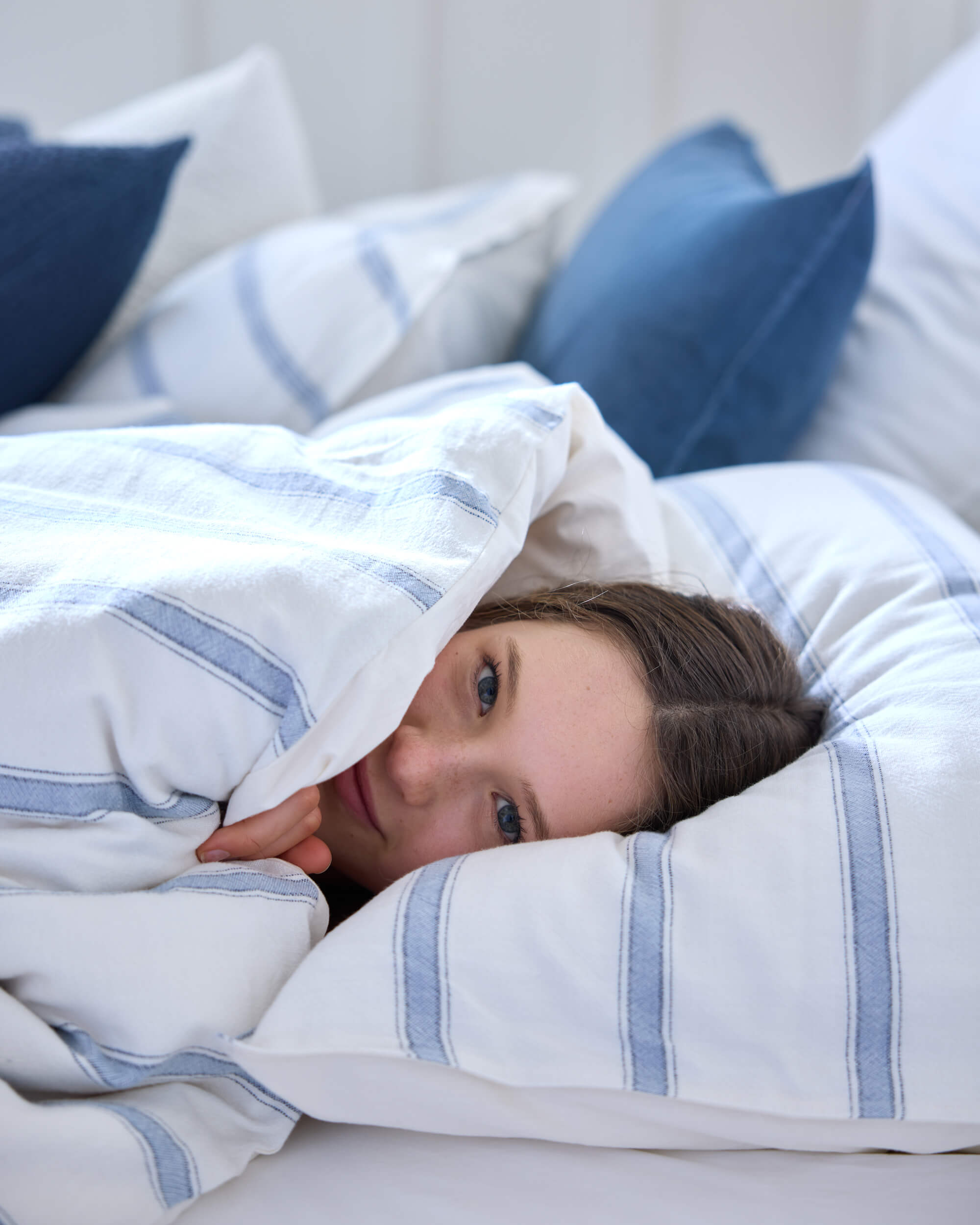 Royal Doulton Kate duvet cover with pale blue stripes styled on a bed with a person tucked under the bedding