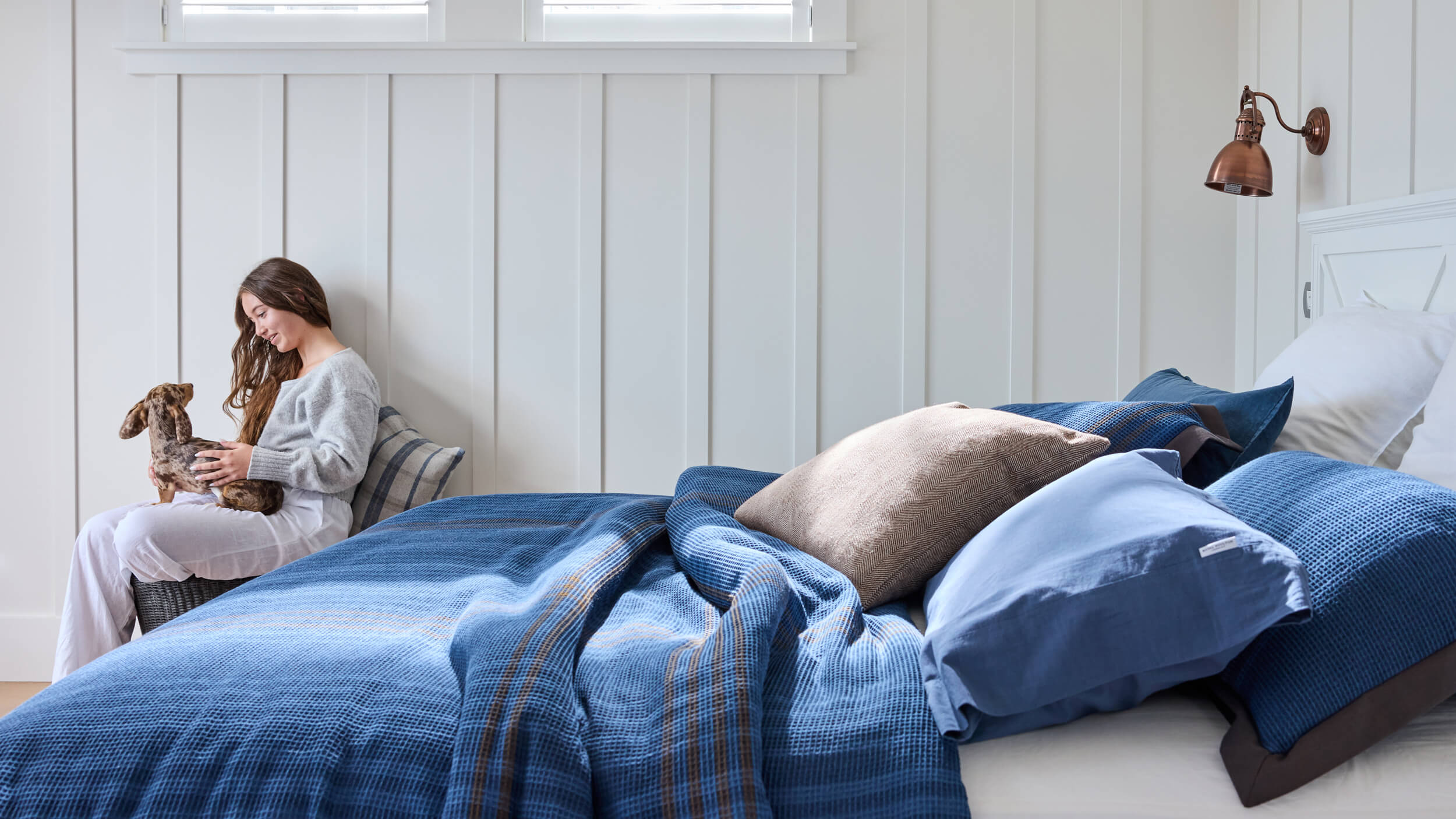Royal Doulton Hampshire blue check bedding styled on a bed beside a woman holding a small dog